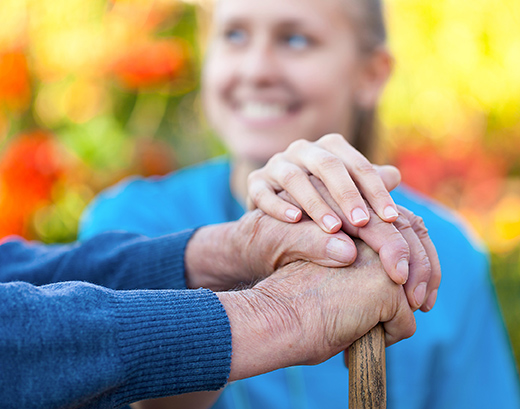 Eine junge Frau legt eine Hand auf zwei übereinandergelegte Hände eines Seniors