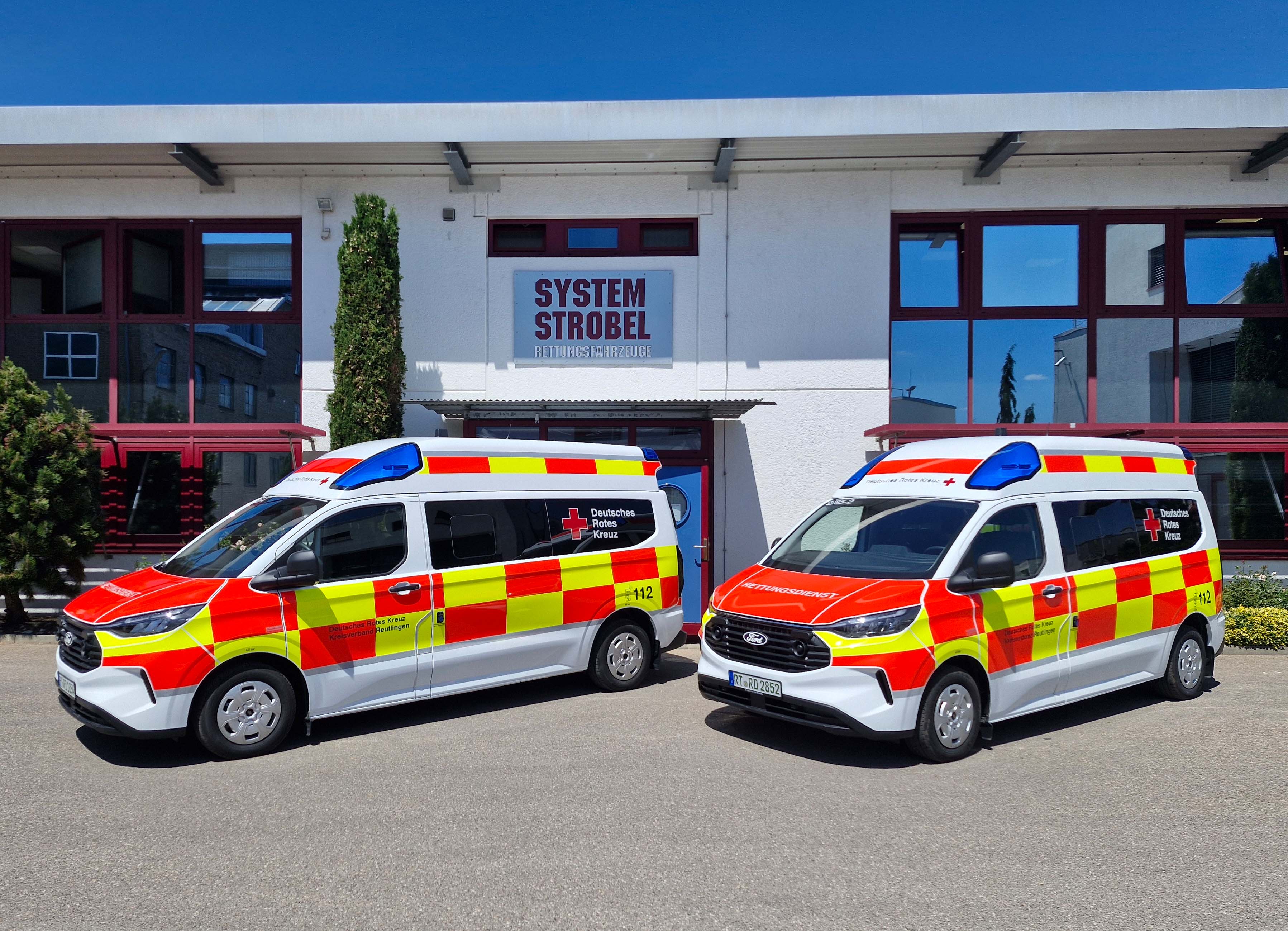 Das Bild zeigt die zwei neuen Krankentransportwagen vor dem Gebäude der Firma Strobel, der die Fahrzeuge ausbaut. 