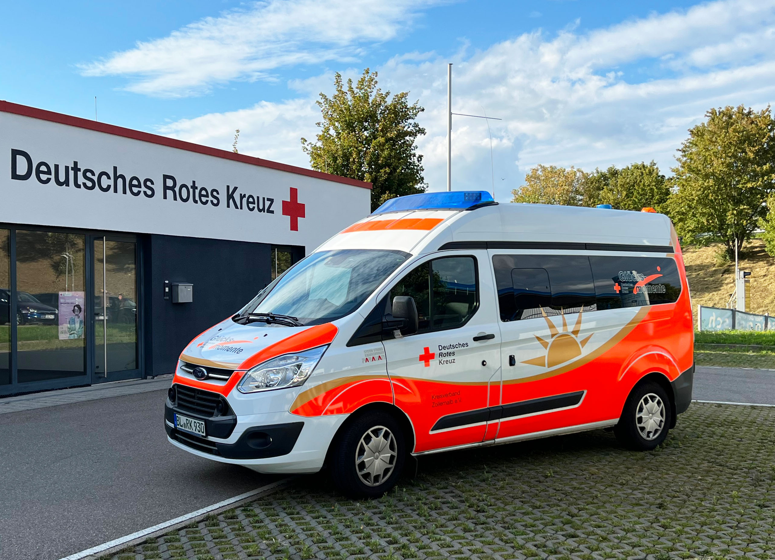 Bild: Das Glücksmomente-Fahrzeug steht vor einem DRK Gebäude. übergeben den Spendenscheck an DRK-Kreisgeschäftsführer Thomas Födisch