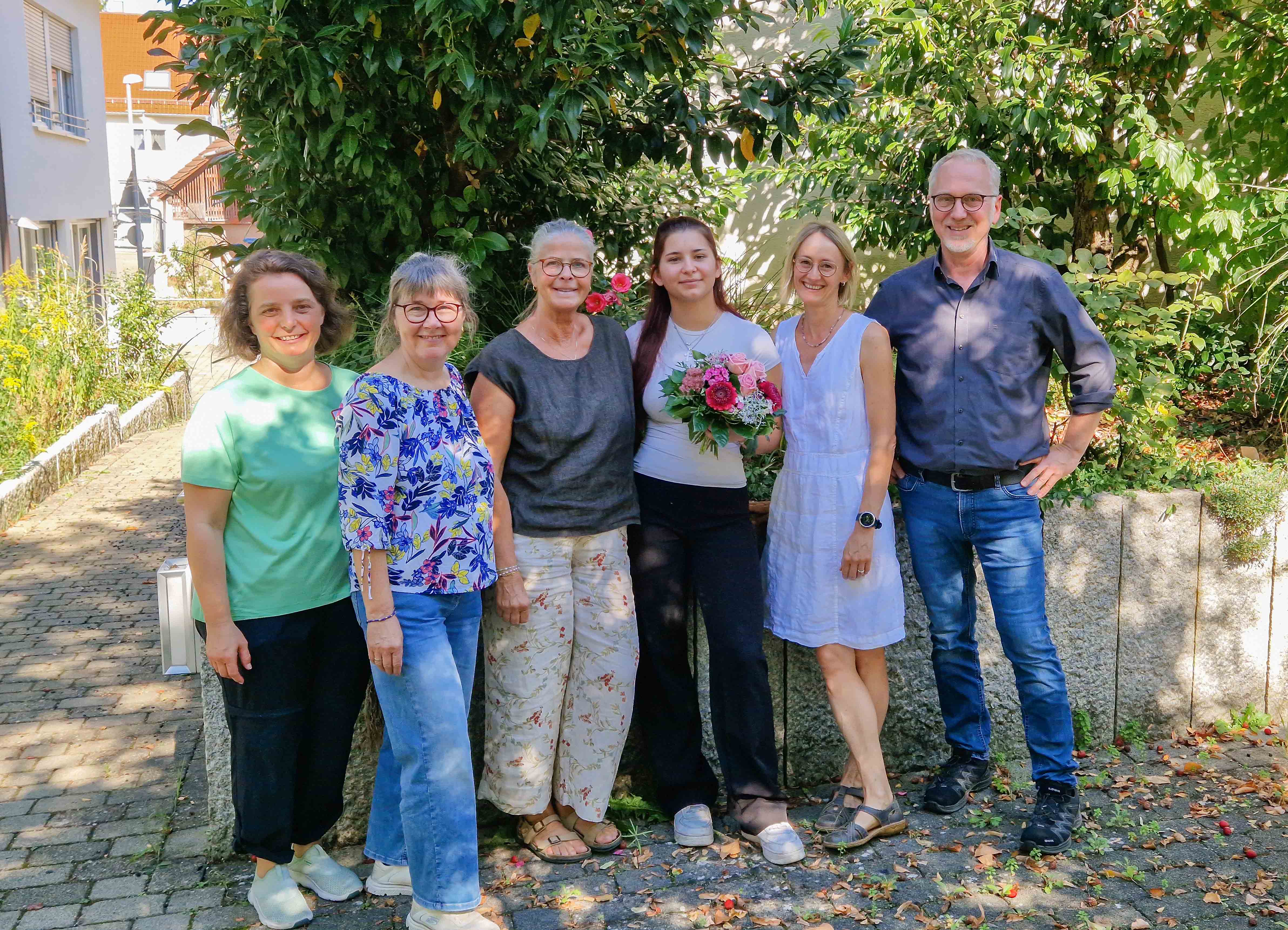 Bild: Die mitarbeitenden der Tagespflege stehen mit Elena im Garten