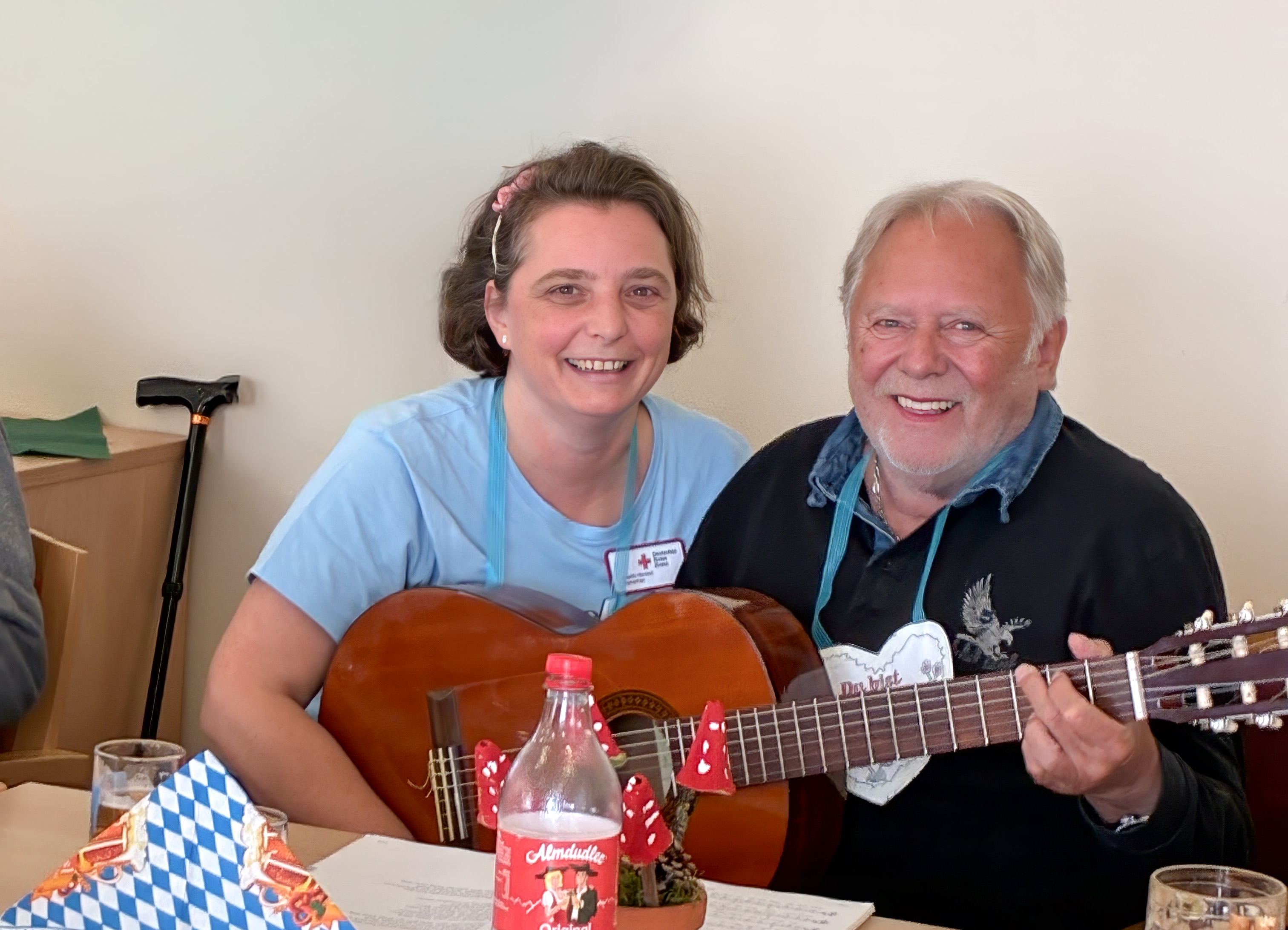 Bild: eine Frau und ein Mann sitzen am Tisch und spielen Gitarre und lachen dabei. 