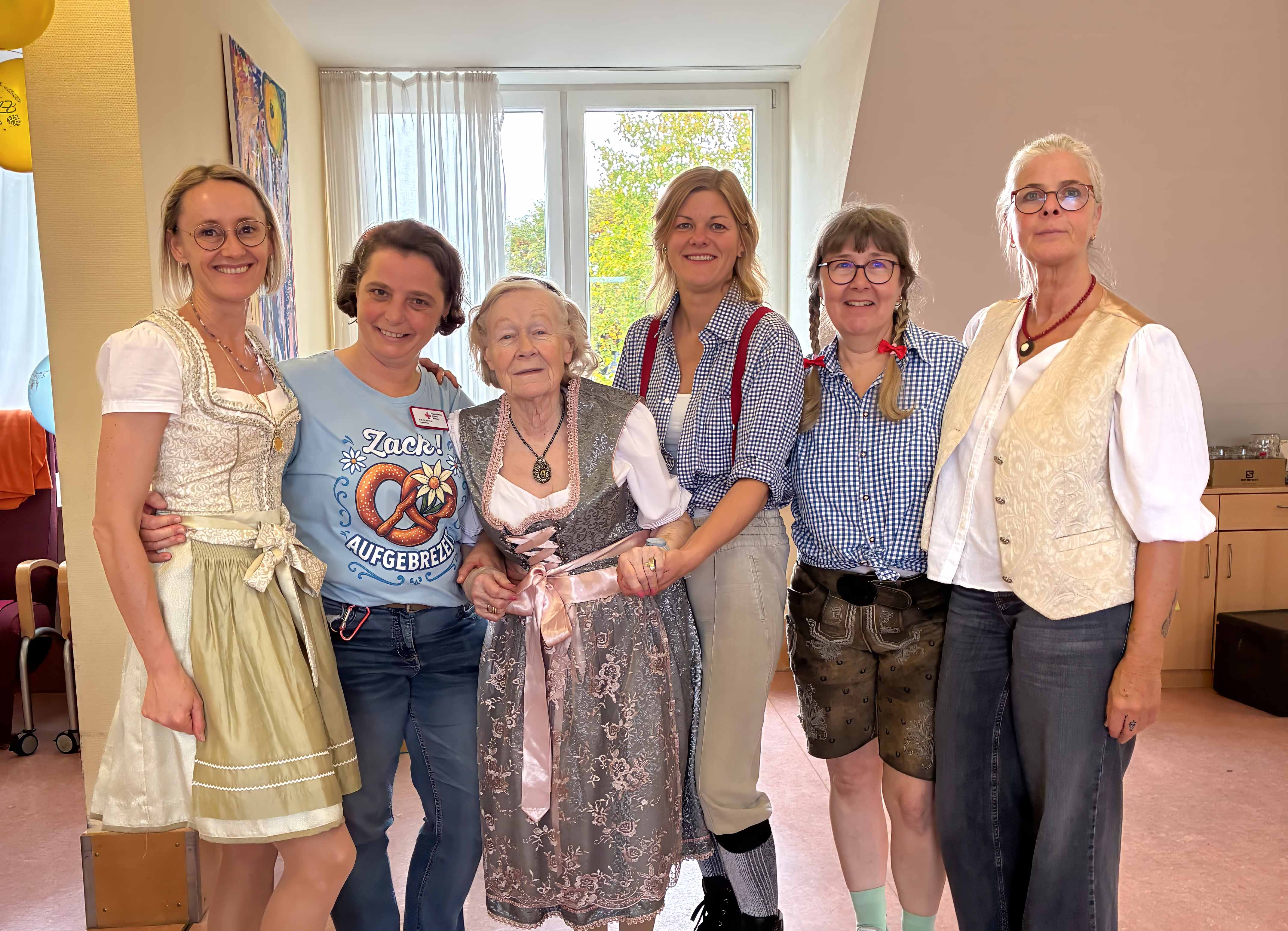 Bild: Mitarbeiterinnen und Tagesgast bekleidet mit einem Dirndle oder einer Lederhose stehen zusammen. 