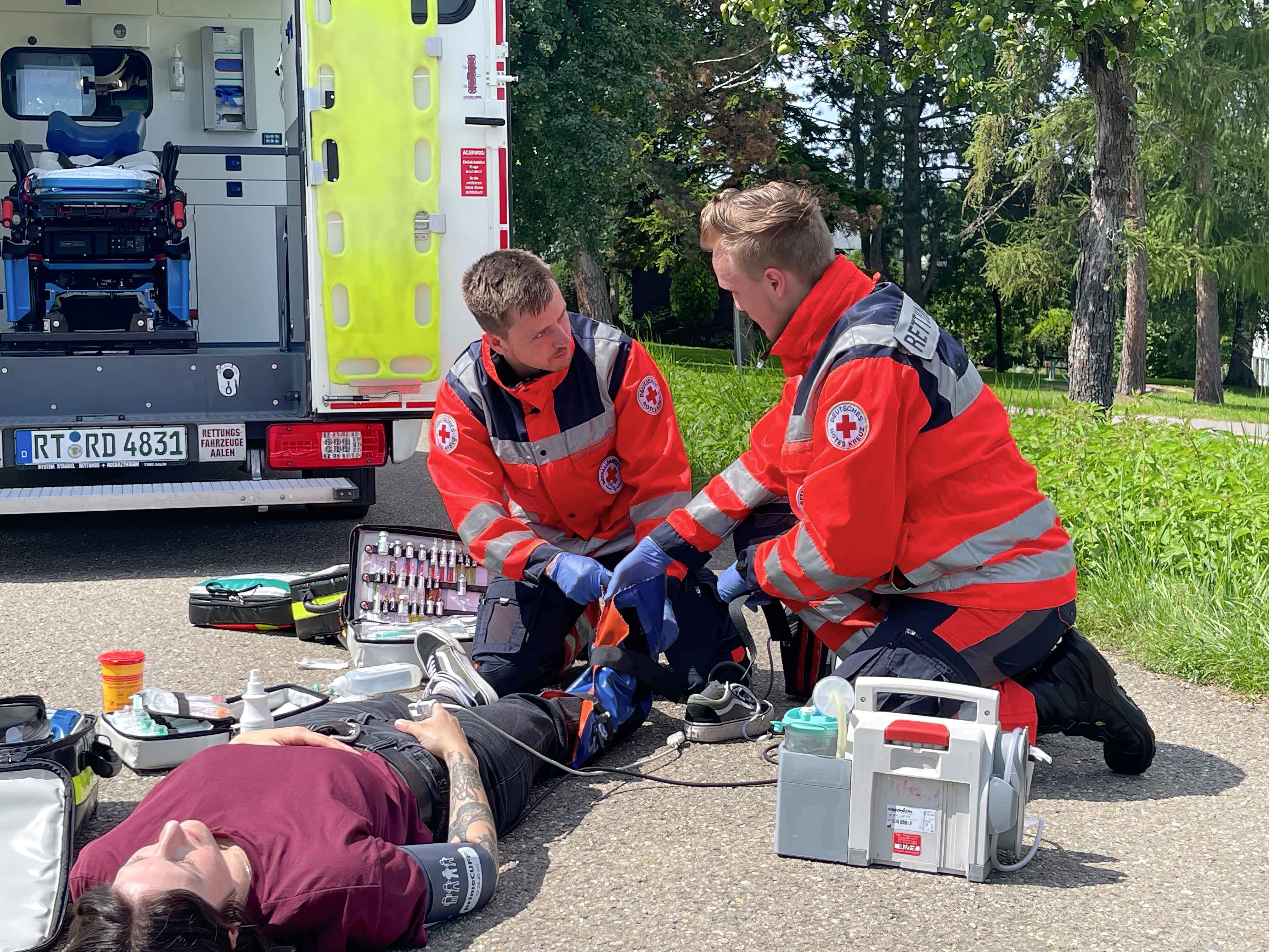 Eine verletzte Frau liegt am boden und wird von 2 Notfallsanitäter versorgt